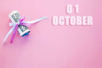 calendar date on pink background with rolled up dollar bills pinned by pink and blue ribbon with copy space. October 1 is the first day of the month
