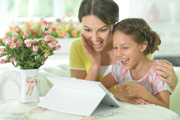 happy mother and daughter using tablet together at home