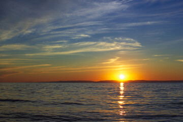 Scenic sunset on Lake Baikal in dark moody colors with blue sky, the bright sun sets over the horizon above calm waves
