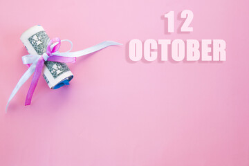 calendar date on pink background with rolled up dollar bills pinned by pink and blue ribbon with copy space. October 12 is the twelfth day of the month