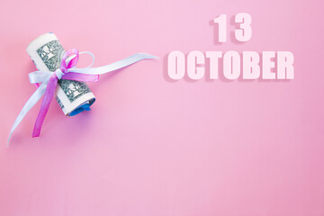 calendar date on pink background with rolled up dollar bills pinned by pink and blue ribbon with copy space. October 13 is the thirteenth day of the month