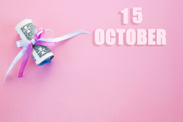 calendar date on pink background with rolled up dollar bills pinned by pink and blue ribbon with copy space. October 15 is the fifteenth day of the month
