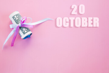 calendar date on pink background with rolled up dollar bills pinned by pink and blue ribbon with copy space. October 20 is the twentieth day of the month
