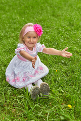 Little girl in beautiful dress sits on the grass and stretches her arms forward