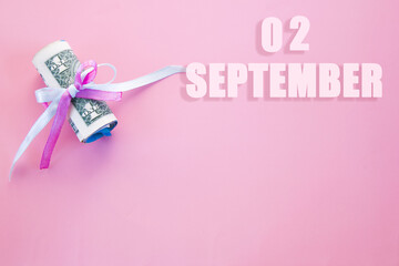 calendar date on pink background with rolled up dollar bills pinned by pink and blue ribbon with copy space. September 2 is the second day of the month
