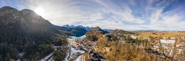 Aerial panorama drone shot of Hohenschwangau by lake in Fussen with view of Alps snow mountain range in Germany winter