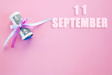 calendar date on pink background with rolled up dollar bills pinned by pink and blue ribbon with copy space. September 11 is the eleventh day of the month