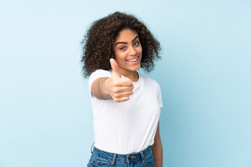 Young African American woman isolated on blue background with thumbs up because something good has happened