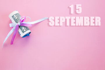 calendar date on pink background with rolled up dollar bills pinned by pink and blue ribbon with copy space. September 15 is the fifteenth day of the month