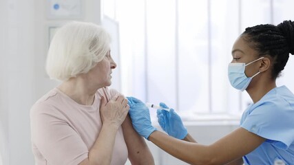 An elderly woman getting a vaccine for coronavirus. Female doctor wearing mask and gloves with a syringe makes an injection to a mature senior patient. Concept of health care, vaccination program. - Powered by Adobe