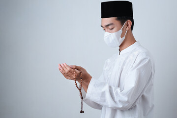 Asian Muslim Man wearing muslim clothes holding prayer beads with medical mask and skull cap...