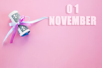 calendar date on pink background with rolled up dollar bills pinned by pink and blue ribbon with copy space. November 1 is the first day of the month