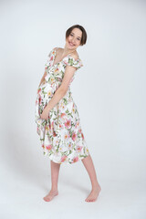 Studio portrait of cheerful young pregnant woman in summer dress on white gray background, happy pregnancy concept