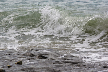 pebble stones on the sea beach, the rolling waves of the sea with foam