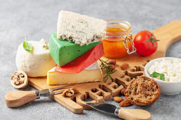 Assortment of different cheese types - brie, blue, green and red pesto on cutting board. Food background.