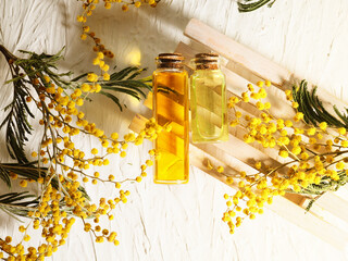 Two bottles of oil on a wooden stand surrounded by mimosa branches, top view, spa and aromatherapy