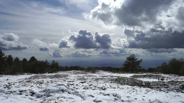 winter view in Sicily of volcanic landscape, old lava snow covered, low clouds at the horizon, panning on Etna Mountain and stone refuge 
