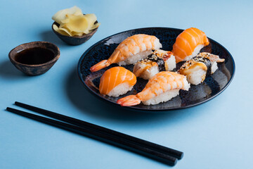 Delicious appetizing sushi set, served on clay plate with soy sauce and chopsticks, flat lay on blue table. Traditional Japanese food, tasty seafood, sushi restaurant concept