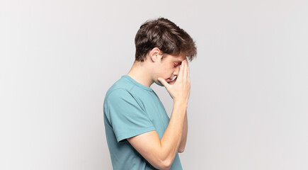 young boy covering eyes with hands with a sad, frustrated look of despair, crying, side view