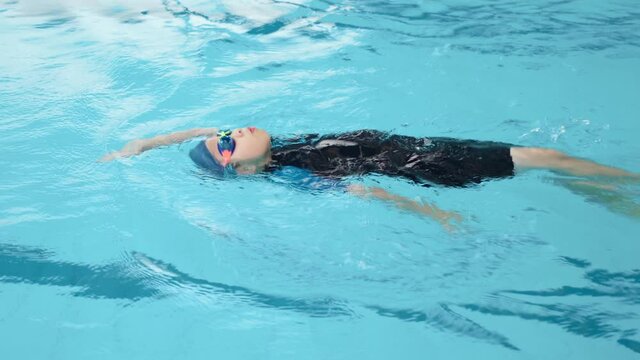 An Asia boy wearing goggles and cap swimming backstroke in the swimming pool. Summer and vacation. Learning with professional in the school. Enjoy and happy with class. Exercise for health 