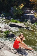 Young woman sitting on cliff edge over fast mountain river on summer or early autumn outdoor