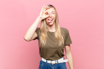 young blond pretty woman smiling happily with funny face, joking and looking through peephole,...