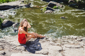 Young woman sitting on cliff edge over fast mountain river on summer or early autumn outdoor