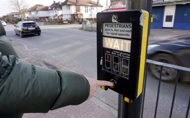 Part of man body wearing green jacket push pedestrian crossing button to cross the road, it shows...