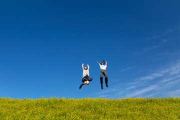 菜の花の咲く土手でジャンプをする男女の高校生。春、入学、お祝い,卒業,合格イメージ