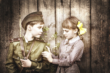 Fototapeta na wymiar Postcard, stylized as vintage for the Victory Day. A boy in a military uniform and a girl in an old dress. The theme of May 9, Victory Day in Russia. Soft selective focus, added noise.