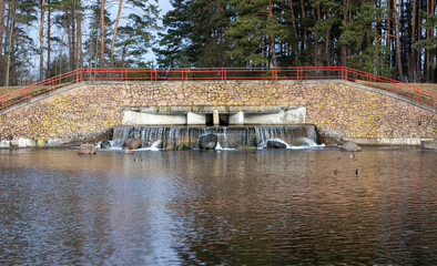 Small waterfall in the city park. Jets of water fall on stones, and ducks swim nearby on the water....