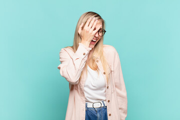 young blond pretty woman laughing and slapping forehead like saying d’oh! I forgot or that was a...