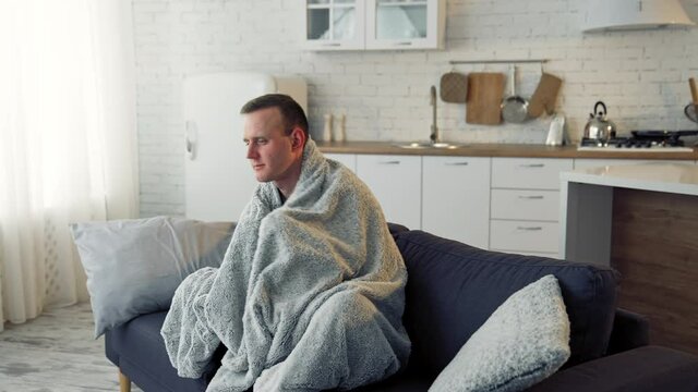 Unwell guy suffering coronavirus infection. Sick man with feeling ill and laying down on bed wrapped in blanket.
