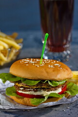 Grilled hamburger with fries and cola on grey background.  Vertically.