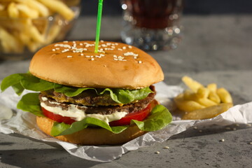 Grilled hamburger with fries and cola on grey background.   Horizontally.