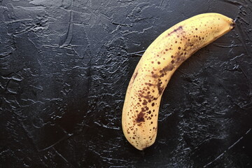 Overripe banana with dark spots on the skin on  blac background .Ugly fruit. Buying imperfect...