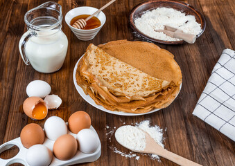 ingredients for making pancakes. flour, eggs, milk, honey. fresh thin pancakes on a wooden table 