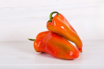 Two bulgarian sweet bell peppers on white wooden background.