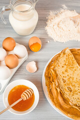 ingredients for making pancakes. flour, eggs, milk, honey. fresh thin pancakes on a wooden table 