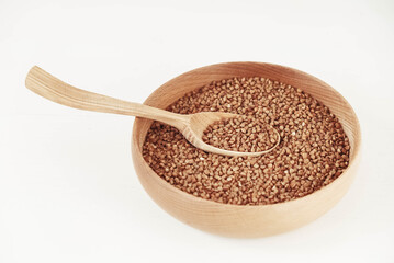 Buckwheat kernels in wooden bowl and spoon on white background. Top view. Copy, empty space for text