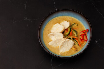 Asian soup with chicken and vegetables: zucchini, red pepper and carrot. Dish isolated in a blue bowl, close-up on a black marble background. Asian cuisine.