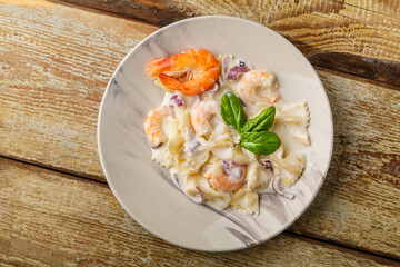 Farfalle pasta with shrimps in a creamy sauce on a gray plate on a wooden table.