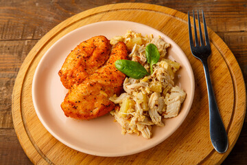 Baked chicken breast in sauce with salad on a plate next to a fork on a wooden table on a round stand.