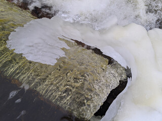 slope of a waterfall in early spring that flows under a canopy of ice
