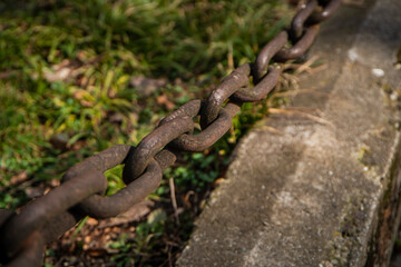 rusty chain, Metal links of a chain, rusty links of a large chain, a fragment of a fence on a background of green grass