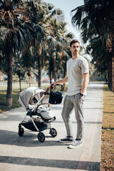 Young handsome father walking with his baby girl in the stroller around green park with palm trees