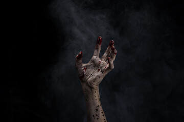Bloody and dirty zombie hand rising up from the soil.  Hand Rising Out Of A Graveyard. Black background and smoke.