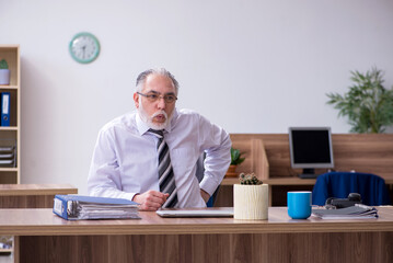 Old male employee suffering from radiculitis at workplace