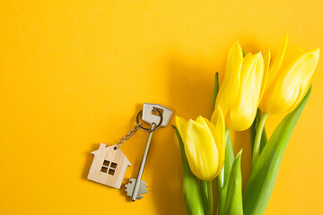 Key ring in the shape of wooden house with key on yellow background and spring tulips. Building, design, project, moving to new home, mortgage, rent and purchase real estate, summer offer. Copy space - obrazy, fototapety, plakaty