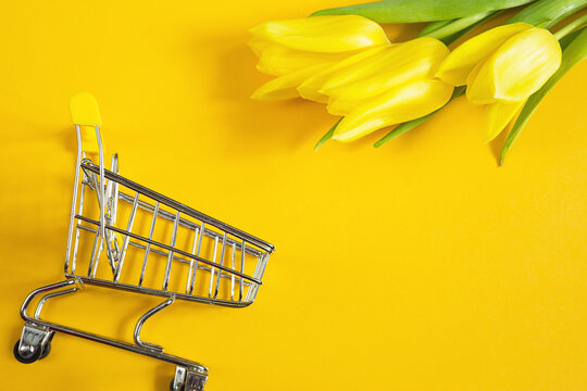 Yellow Tulips On A Solid Color Background And Shopping Cart. Online Shopping In Spring And Summer, Buying Gifts For The Holidays, Easter, Women's Day, March 8. Flower Shop, Floristry. Copy Space